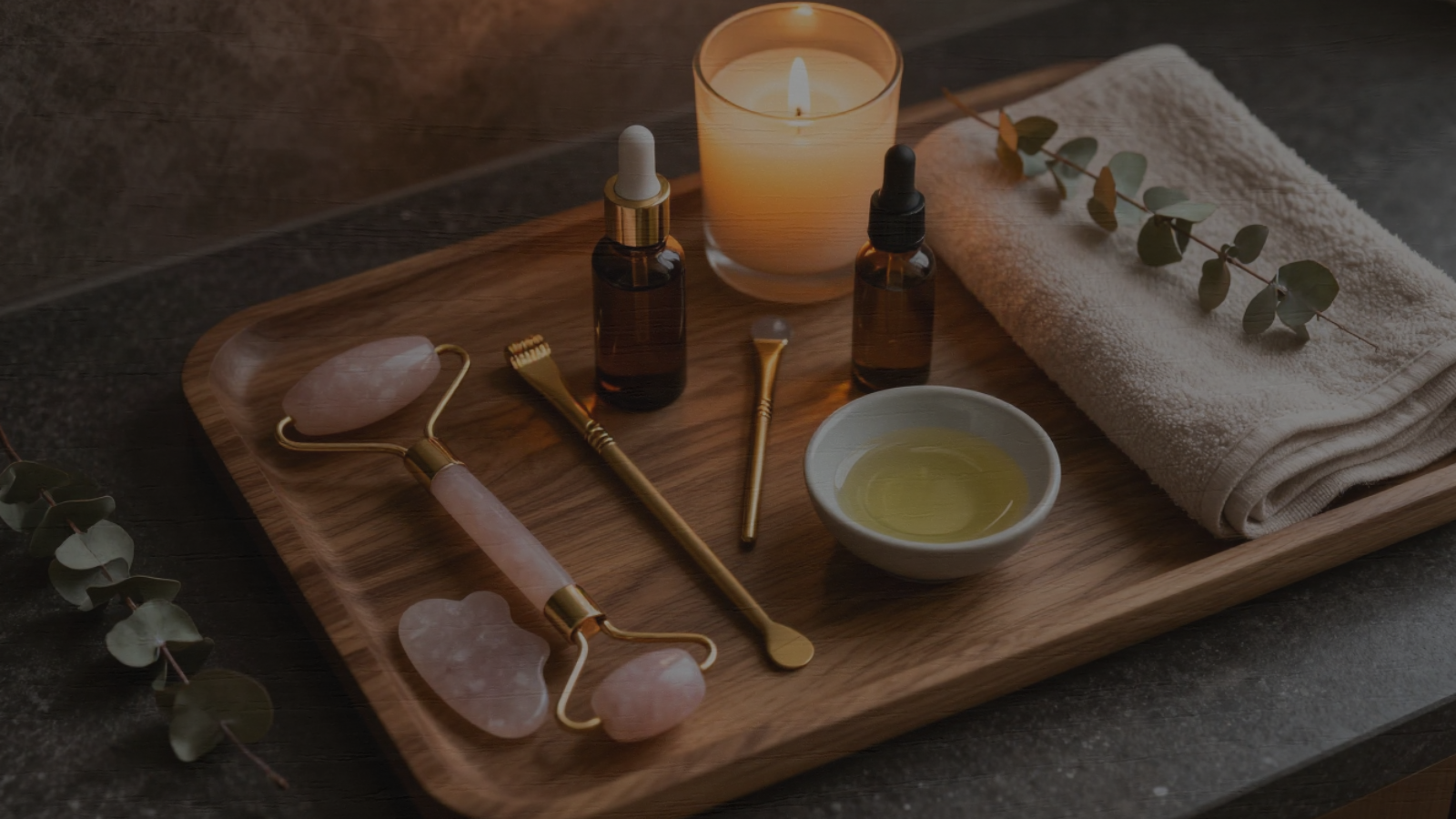 Facial rollers, gua sha tools, skincare oils, candle, and towel arranged for an at-home Luvoskin skin recovery ritual.